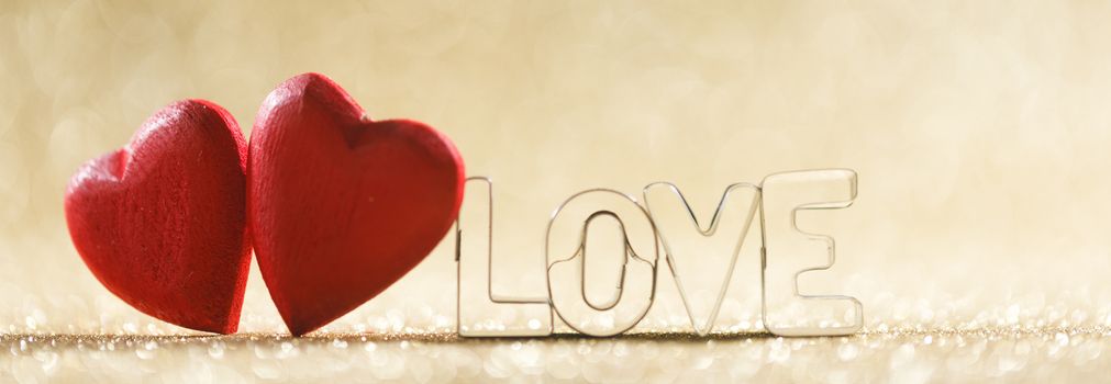 Two red handmade wooden hearts and word love on golden bright glitter lights bokeh background