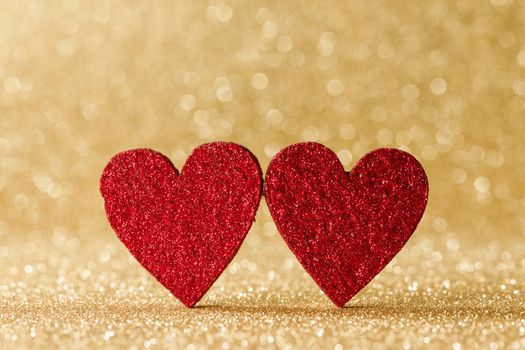 Two small handmade red glitter hearts on bright golden lights bokeh background Valentines day card