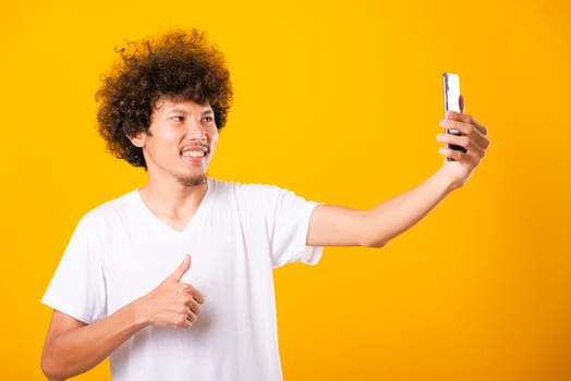 Portrait asian handsome man curly hair taking selfie with mobile phone isolated on yellow background