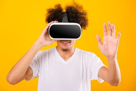 Asian handsome man with curly hair he using virtual reality headset or VR glass isolate on yellow background