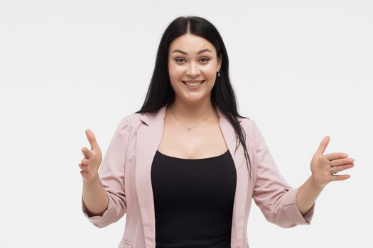 Positive optimistic young female in casual clothes gesturing and showing big size with hands while standing against white background