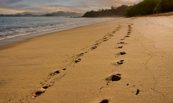 Footsteps along an empty beach in early morning light