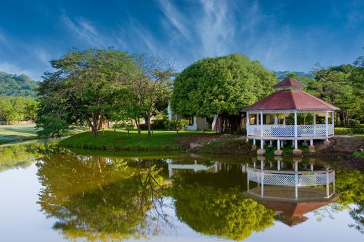 A white gazebo and trees on the edge of a lake and golf course with reflections