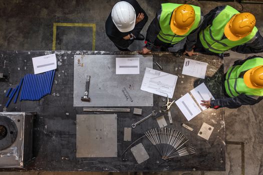 Team of workers and foreman look at documents and blueprints on table at factory top view