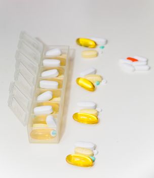 A daily dose pill container with pills and vitamins on a white counter