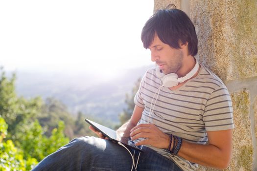 young man working with a tablet pc listening music with headphones, outdoor