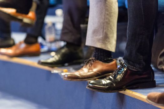 Detail of row of men's formal corporate business shoes. Unrecognizable business people sitting in conference hall at business event. Business and Entrepreneurship concept.