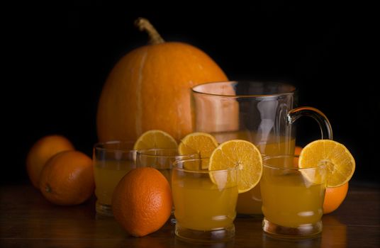 glass of delicious orange juice with oranges and a pumpkin on a table, studio picture