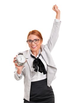 Saving time concept. Success concept. Beautiful excited young businesswoman in a suit holding an old fashioned alarm clock with the other arm raised in celebration, isolated on white background.