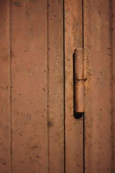 Detail of the hinge of a brown metal door, rusted and ruined by weather and bad weather. Vertical shot.