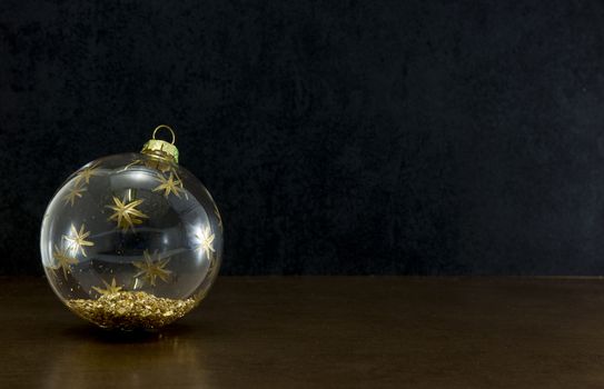 transparent christmas ball with gold colored glitters on a dark black background for christmas card