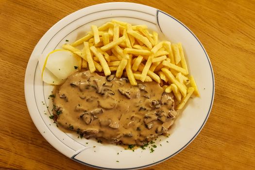 Jaeger Viennese schnitzel with French fries and mushrooms close-up on a plate. horizontal top view from above