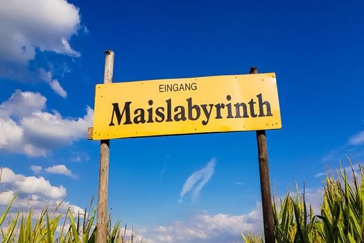 Corn Maze is a maze cut from a corn field. Maize labyrinths are popular with tourists and children. Entrance sign in front of blue sky with lettering in german - entrance Maislabyrinth