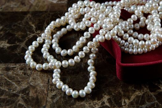 Pearl necklace in a red heart-shaped gift box on a marble background. Close-up. Happy birthday or mother's day. A romantic gift for Valentine's Day or for a wedding