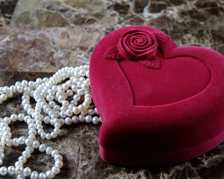 Pearl necklace in a red heart-shaped gift box on a marble background. Close-up. Happy birthday or mother's day. A romantic gift for Valentine's Day or for a wedding