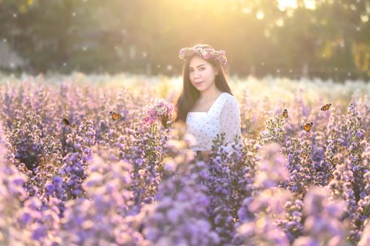 A woman watching flowers in a flower field with butterflies in the evening, orange light.