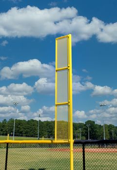A bright yellow foul ball pole in a baseball field against blue sky