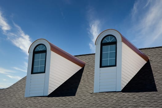 Two dormers on a roof against blue sky