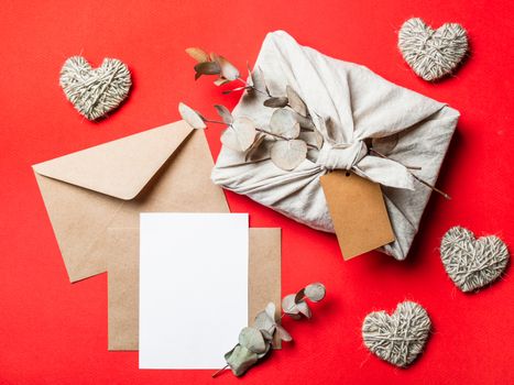 Zero waste Valentine's Day concept and mock up on red. Eco-friendly gift cloth wrapping in Furoshiki style, craft paper envelope,empty greetings card. Top down view or flat lay. Copy space for design