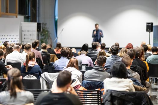 Speaker giving a talk in conference hall at business event. Audience at the conference hall. Business and Entrepreneurship concept. Focus on unrecognizable people in audience.