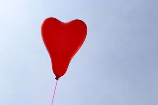 The picture shows a red heart balloon in front of the blue sky