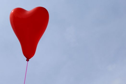 The picture shows a red heart balloon in front of the blue sky