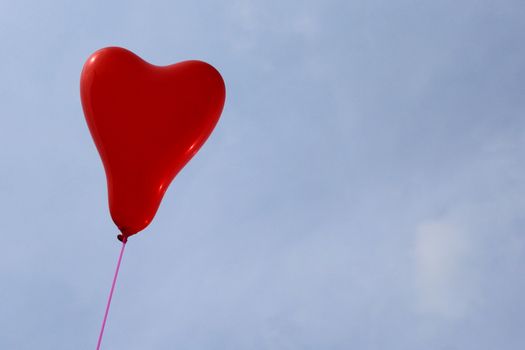 The picture shows a red heart balloon in front of the blue sky