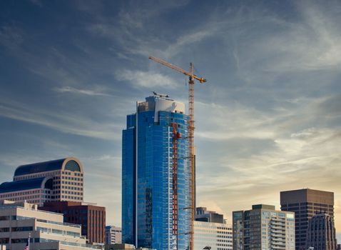 A blue office tower in city skyline with yellow construction crane
