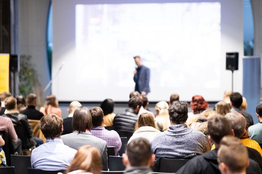 Speaker giving a talk in conference hall at business event. Audience at the conference hall. Business and Entrepreneurship concept. Focus on unrecognizable people in audience.