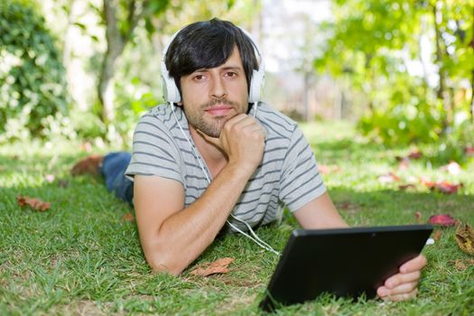 young man relaxing with a tablet pc listening music with headphones on a the park, outdoor