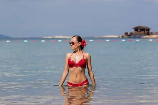 Beautiful woman walking in sea waterLovely young lady in red knitted swimwear looking away and walking in sea water while relaxing in wonderful resort