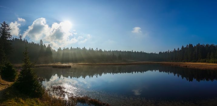 Autumn morning at lake, sun rays glowing through mist, black lake - crno jeyero, Pohorje, Slovenia