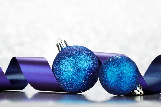 Blue Christmas balls and ribbon on abstract glitter silver background