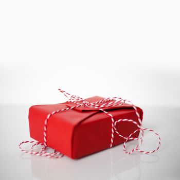 Christmas gift box wrapped in red paper and bow of dtriped rope on white background
