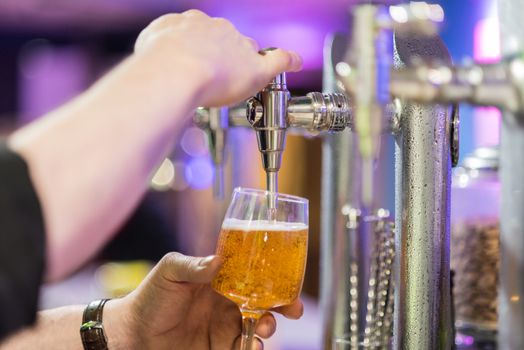 Bartender pouring lager beer in a glass. Shallow dof, selective focus.