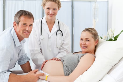 Pregnant woman with her husband and the nurse looking at the camera