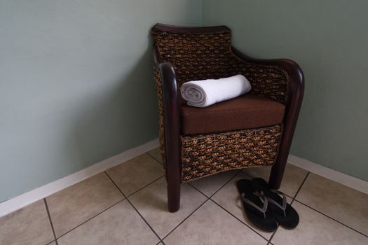 A rattan and wood armchair with clean rolled white towel and shower slippers sauna spa concept, South Africa