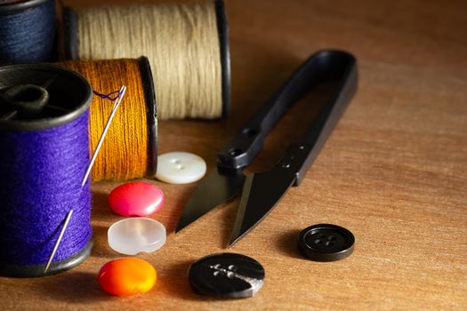 Needle and threads against plastic button and thread cutting scissors on wooden table. Close Up and copy space for text. Concept of tailor or Designer.