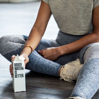 A black African American woman siting down on floor & holding a small water carton.This image was taken on FEB 2015, At a apartment in New York.