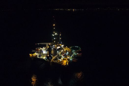 Drilling platform in the port. Oil platform at night in the light of its own lighting. Towing of the oil platform.