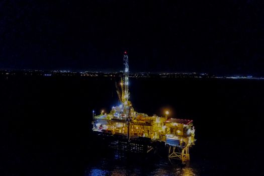 Drilling platform in the port. Oil platform at night in the light of its own lighting. Towing of the oil platform.