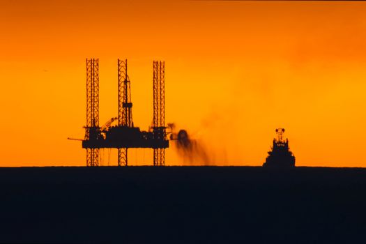 Drilling platform in the port. Oil platform at sunset with a burning torch. Towing of the oil platform.