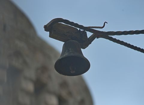 Small black bell hanging and sky and stone fortress in background