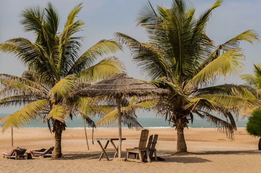 Two chairs and coffee table under a palm leaf and wood parasol on Bijilo Beach in The Gambia