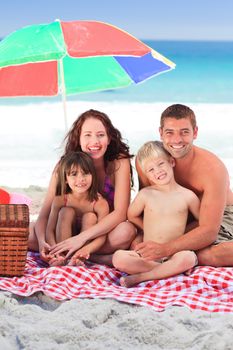 Family picnicking under a sol umbrella on the beach