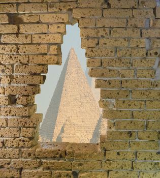 Old yellow brick wall in ruins with a big opening in it viewing on some egyptian pyramids