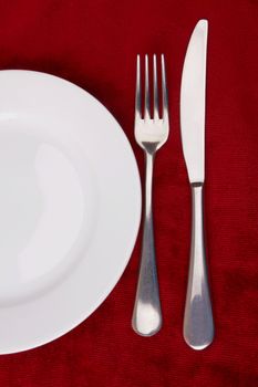 White plate, fork and knife on red background. 