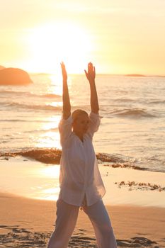 Woman practicing yoga during the sunset against the sea