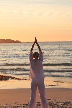 Woman practicing yoga during the sunset against the sea