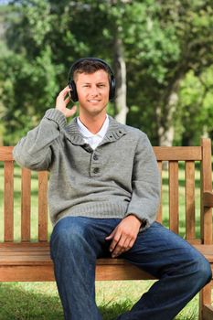 Young man listening to some music on the bench during the summer